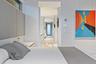 Modern primary bedroom featuring a neutral color palette with light wood-finish flooring, contemporary headboard wall with integrated lighting, and di