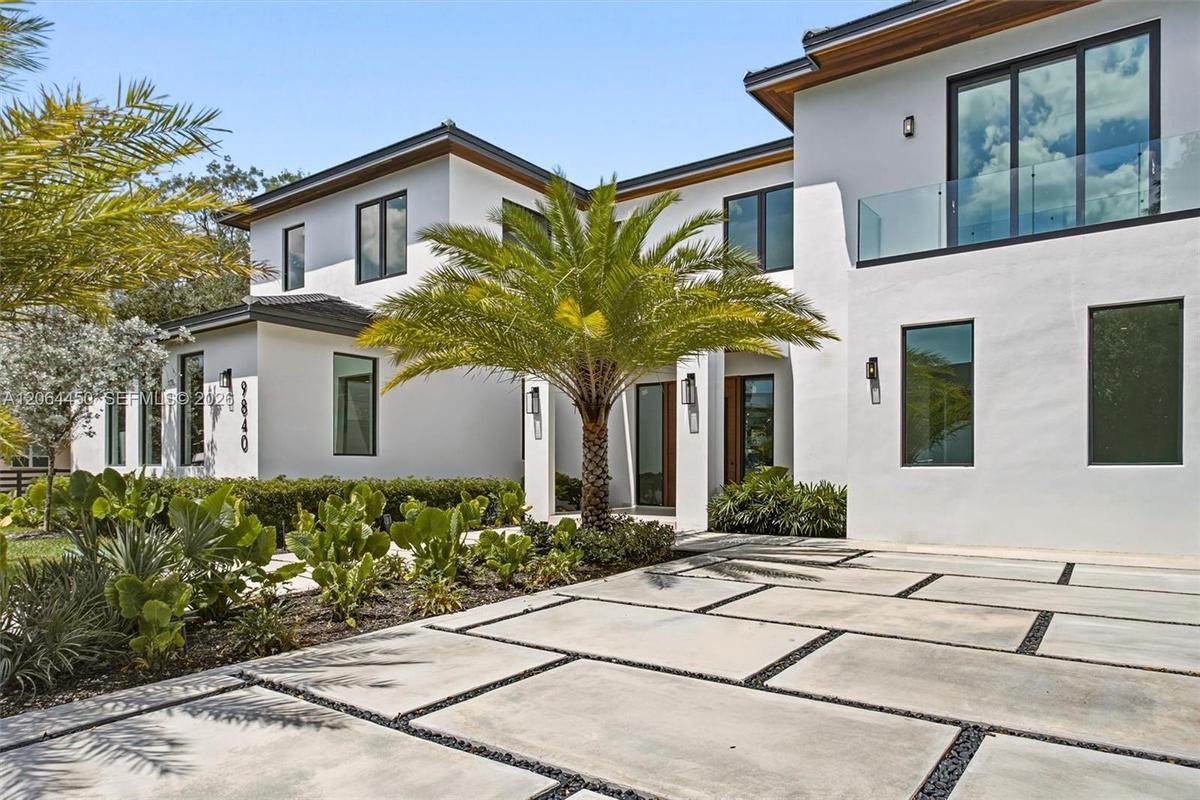 Two-story modern exterior featuring a smooth white stucco finish, dark-framed windows, a flat tile roof, and a horizontal privacy fence