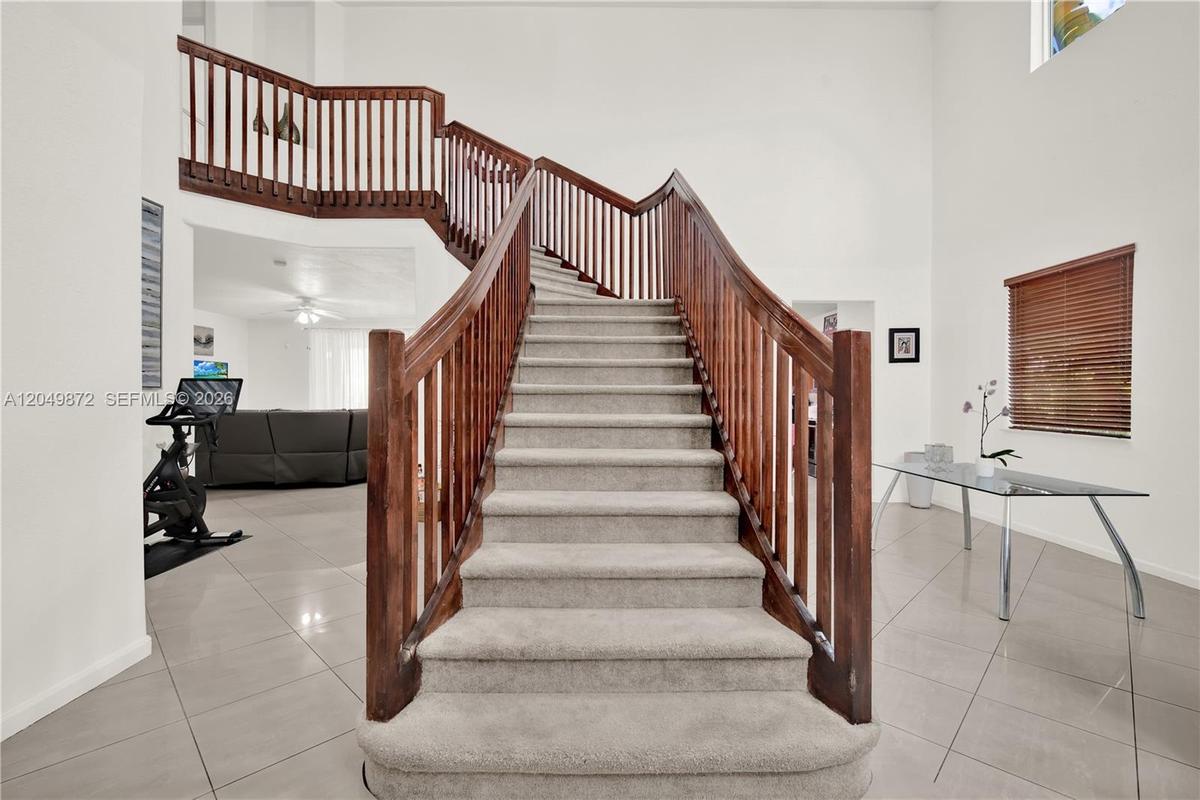 Two-story interior featuring high ceilings, neutral tile flooring, arched windows, and a wooden staircase railing