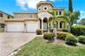 Two-story stucco exterior featuring a turreted entry, decorative arch detailing, two-car garage, and patterned paver driveway