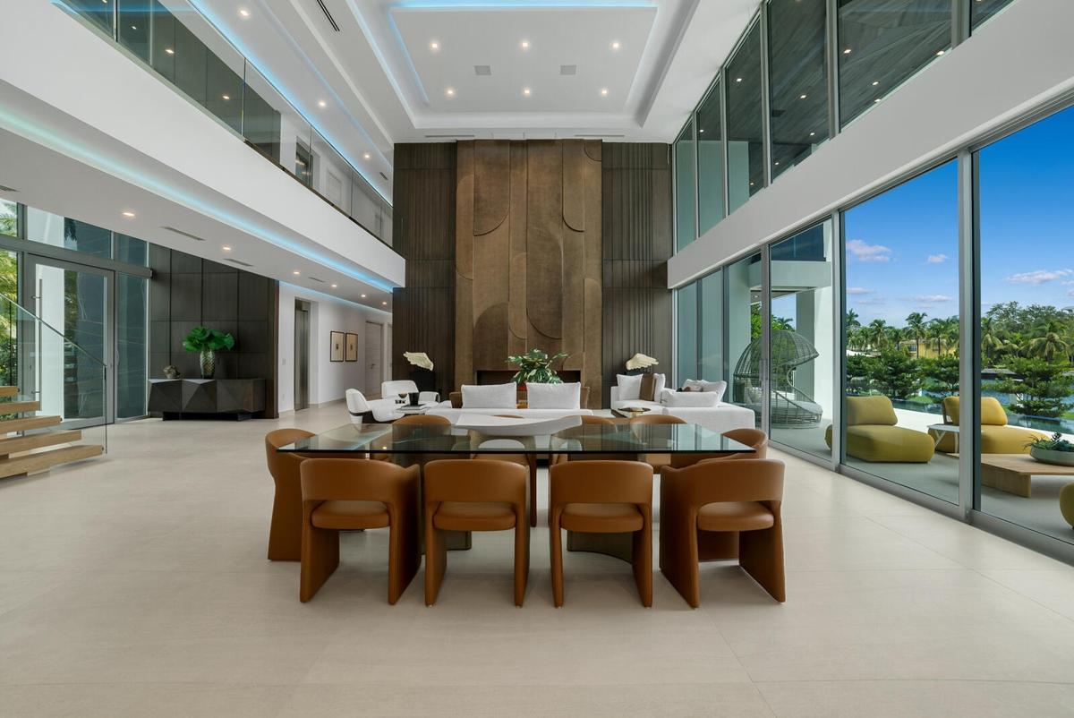 Elegant dining area surrounded by floor-to-ceiling glass, overlooking the waterfront and anchored by the magnificent three-level paneled fireplace wal