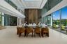 Elegant dining area surrounded by floor-to-ceiling glass, overlooking the waterfront and anchored by the magnificent three-level paneled fireplace wal