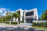 Right-side exterior view showcasing bold contemporary architecture, dramatic floor-to-ceiling glass, a sleek garage, private motor court, and lush tro