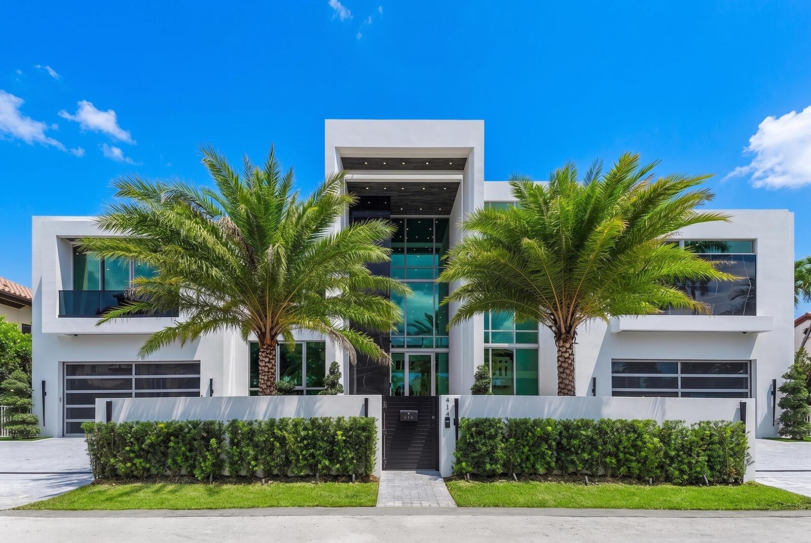 Striking modern architecture with dramatic floor-to-ceiling glass, dual garages, lush tropical landscaping, and an impressive grand entrance.