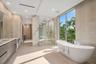 Spa-inspired primary bathroom with a sculptural freestanding tub, expansive windows, dual vanities, and an oversized glass shower wrapped in book-matc
