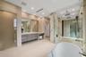 Luxurious primary bath showcasing an oversized glass-enclosed shower with dual rain heads, book-matched stone, floating vanities, and a dedicated make