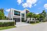 Left-side exterior view showcasing the home’s bold modern architecture, expansive floor-to-ceiling glass, sleek garage, gated motor court, and lush tr