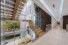 Second-floor landing showcasing the floating staircase from both sides, framed by soaring windows, glass railings, and rich wood-paneled accent walls.