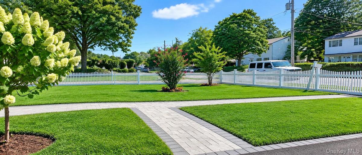 Manicured lawn with a paver walkway, trees, and a white picket fence