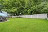 Wide view of the fenced backyard bordered by mature trees.