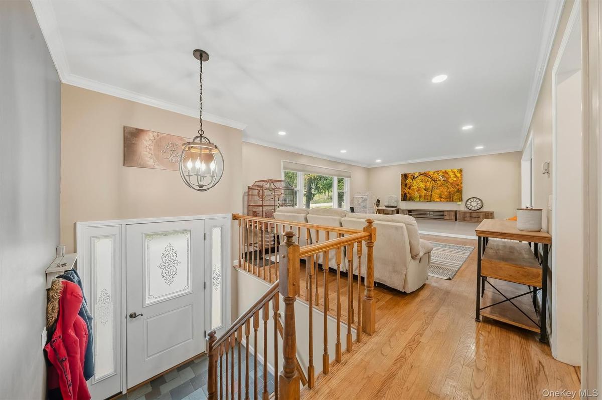 Hardwood flooring, white crown molding, recessed lighting, white entry door with decorative glass panels, and a wood railing