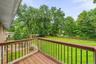 Outdoor deck with wood-finish flooring and black metal railings, overlooking an expansive grass lawn with mature trees and a wood split-rail fence