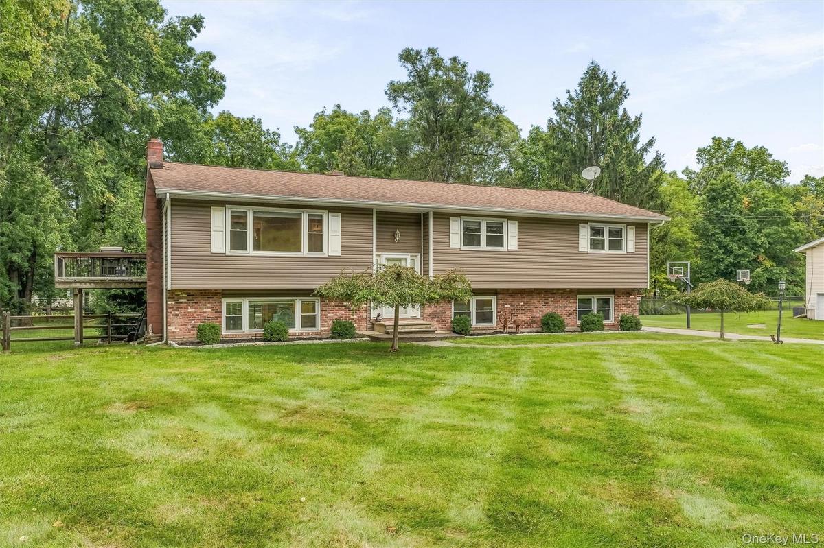 Two-story residence featuring composite siding, brick façade, multiple windows with shutters, an elevated outdoor deck, and established lawn with matu