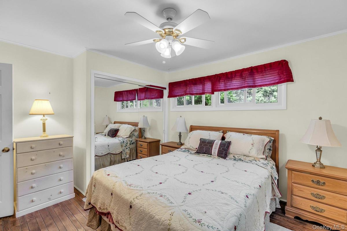 Hardwood flooring, ceiling fan with integrated lighting, built-in mirrored closet, and a horizontal window
