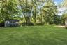 Expansive lawn with mature trees, a detached storage shed featuring double doors, and a gravel area