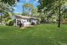 Expansive green lawn, mature trees, white siding exterior, brick patio, and a privacy fence