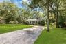 Mature landscaping with towering shade trees frames this single-story residence, set on expansive grounds with a manicured lawn