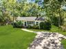 Ranch-style residence featuring white siding, green window shutters, and mature trees