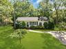 White exterior with dark green shutters, a paved driveway, a concrete pathway, a shingle roof, and mature trees