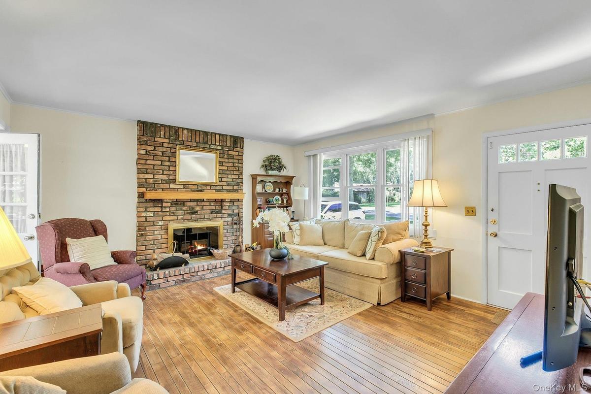 Living room featuring wood-finish flooring, a brick fireplace with a wood mantle, a multi-pane window, and a white entry door with upper glass panels