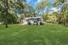 Expansive green lawn, mature trees, white siding exterior, shingle roof, and a paved patio area