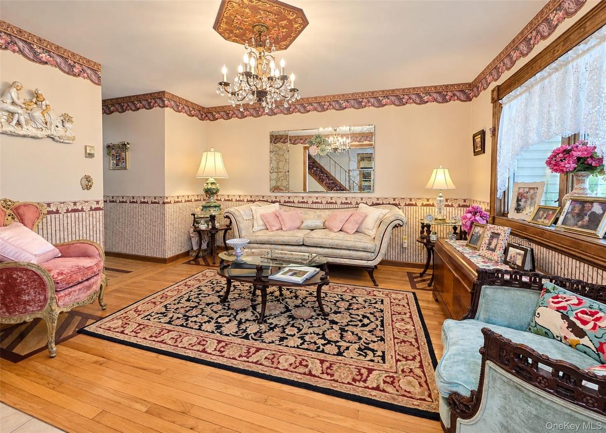 Hardwood flooring with decorative inlay, chandelier with ornate ceiling medallion, decorative wall coverings, window with lace curtain, and built-in w