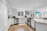 Kitchen with appliances with stainless steel finishes, white cabinetry, light stone countertops, backsplash, and glass insert cabinets
