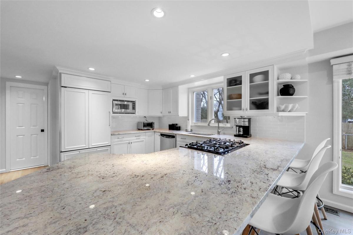 Kitchen featuring glass insert cabinets, a peninsula, a breakfast bar area, light stone countertops, and recessed lighting