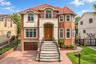 Red brick exterior with a terracotta tile roof, prominent arched entryway, a stone balustrade balcony, and a paved driveway with a garage door