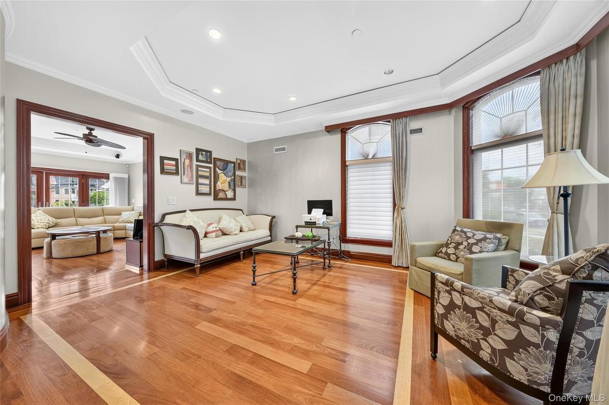 Hardwood flooring with a decorative inlay, tray ceiling with recessed lighting, and arched windows with detailed muntins