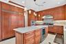 Custom wood cabinetry, stainless steel appliances, central island with integrated beverage refrigerator, light-toned countertops, and recessed and pen