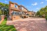 Brick exterior with a tile roof, featuring a paver driveway, wrought iron balcony, and a brick privacy wall with iron fencing