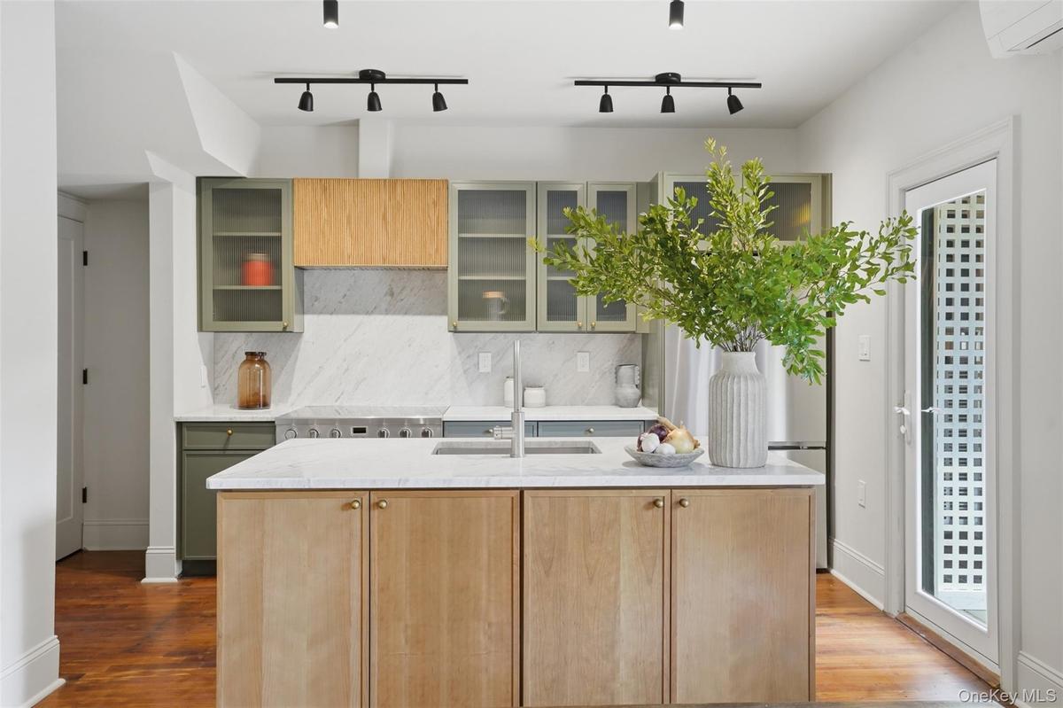 Kitchen featuring a central island with wood-finish cabinetry and a light-toned countertop, a range with a stainless steel cooktop, light-toned backsp