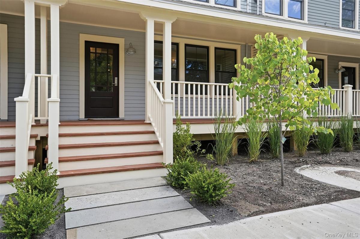 Front exterior featuring a multi-level porch, dark wood-panel door, white porch railings, and a concrete paver walkway