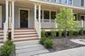 Front exterior featuring a multi-level porch, dark wood-panel door, white porch railings, and a concrete paver walkway