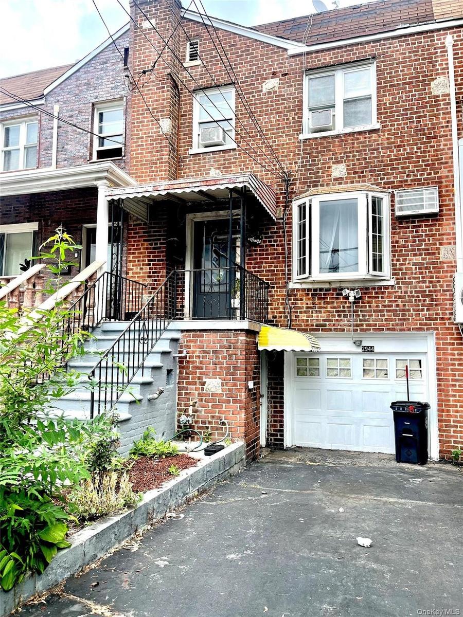 Brick exterior with a second-story bay window, ground-level garage, and covered entryway with wrought iron railings