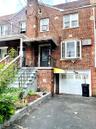 Brick exterior with a second-story bay window, ground-level garage, and covered entryway with wrought iron railings