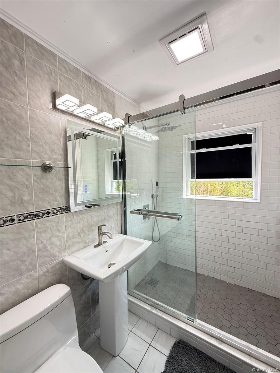 Pedestal sink, wall-mounted vanity lighting, frameless glass shower enclosure, subway tile shower surround, and hexagonal tile shower floor
