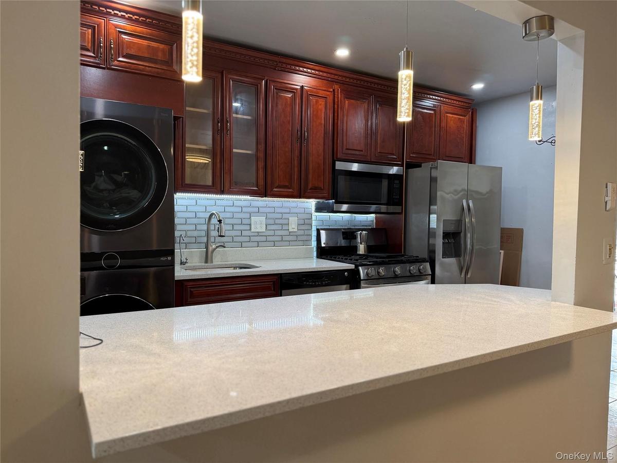 Kitchen featuring light-toned countertops, dark wood-finish cabinetry, stainless steel appliances, and a subway tile backsplash