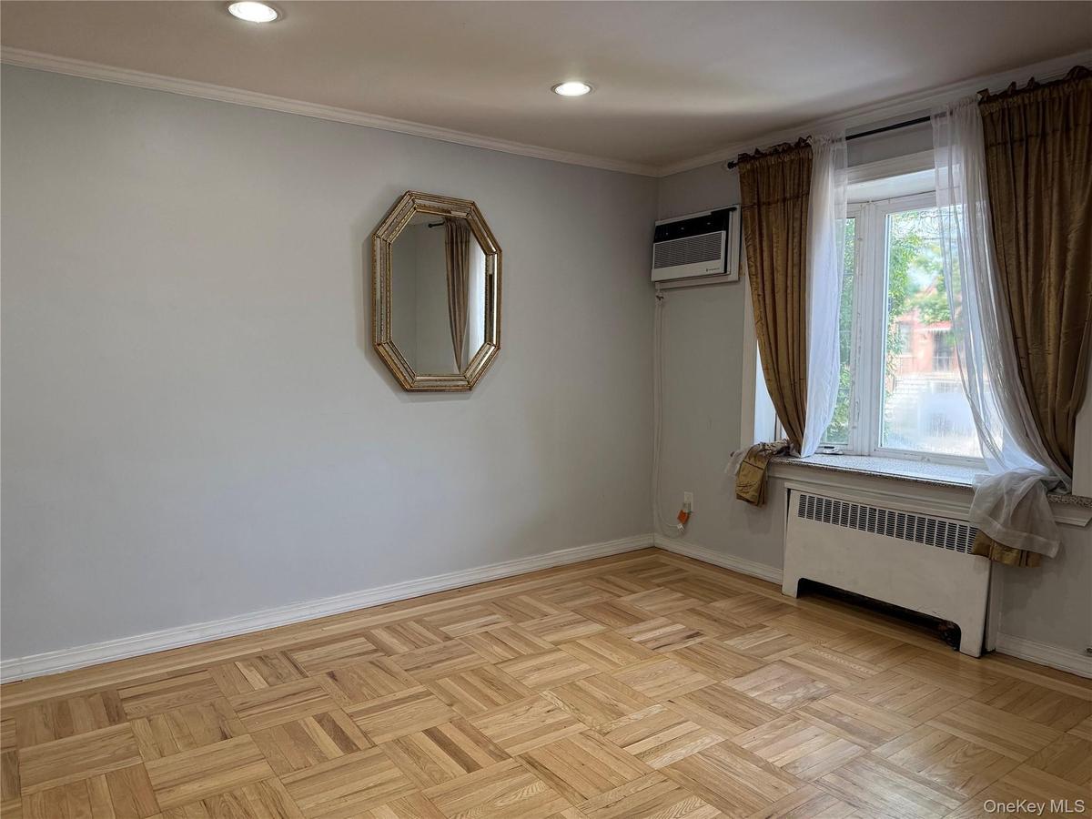 Recessed ceiling lighting, crown molding, parquet wood flooring, window unit air conditioning, and a window with a radiator below