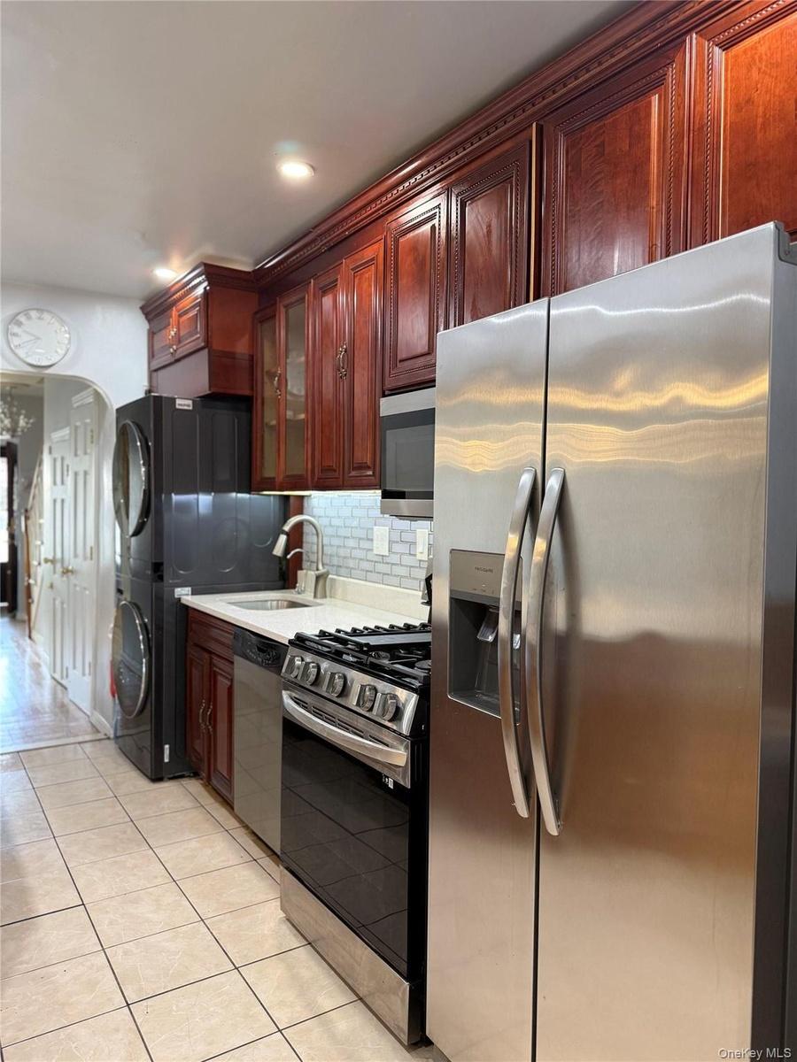 Cherry wood-finish cabinetry, stainless steel appliances, tile flooring, and a subway tile backsplash