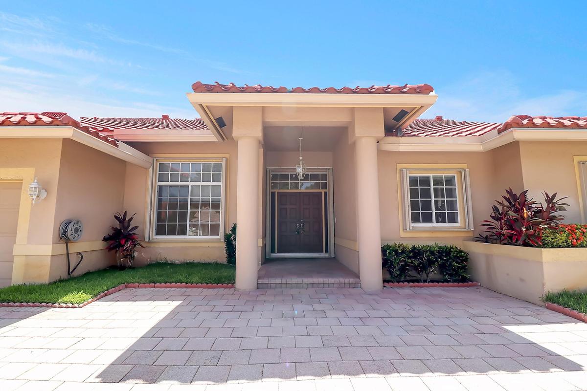 Stucco exterior with a terracotta tile roof, prominent covered entry, decorative double entry doors, paver driveway, and established landscaping