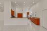 Kitchen and living area featuring white tile flooring, vaulted ceilings, recessed lighting, wood cabinetry, and stainless steel appliances