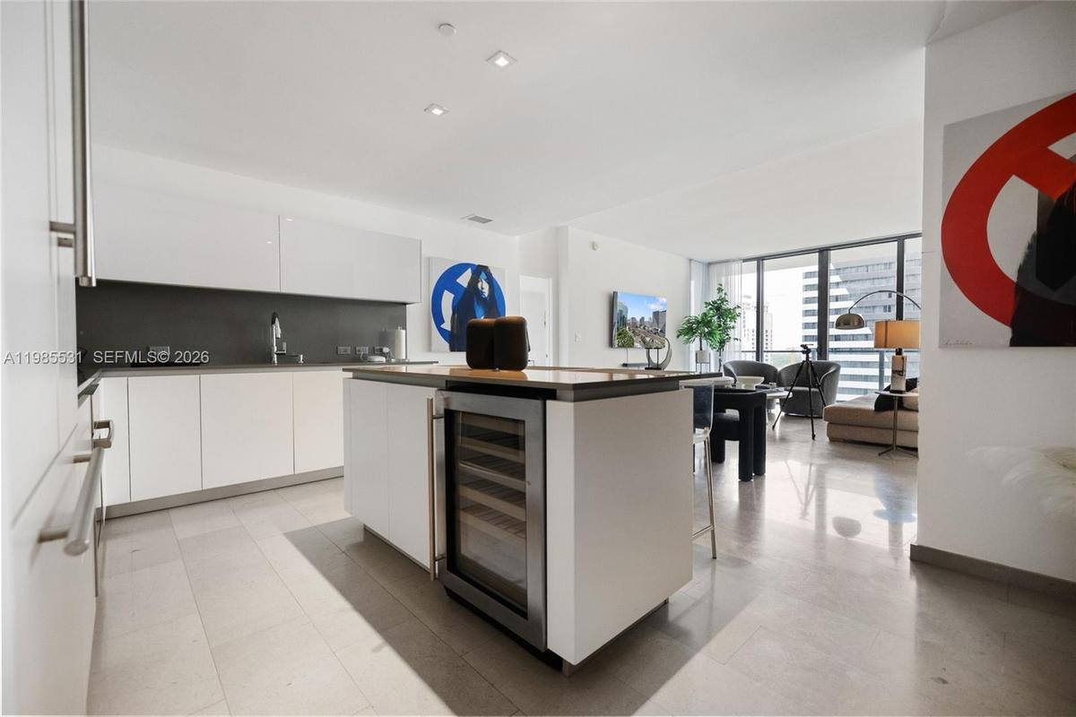 Kitchen featuring flat-panel white cabinetry, grey solid-surface countertops, seamless grey backsplash, stainless steel microwave, and integrated cook