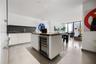 Kitchen featuring flat-panel white cabinetry, grey solid-surface countertops, seamless grey backsplash, stainless steel microwave, and integrated cook