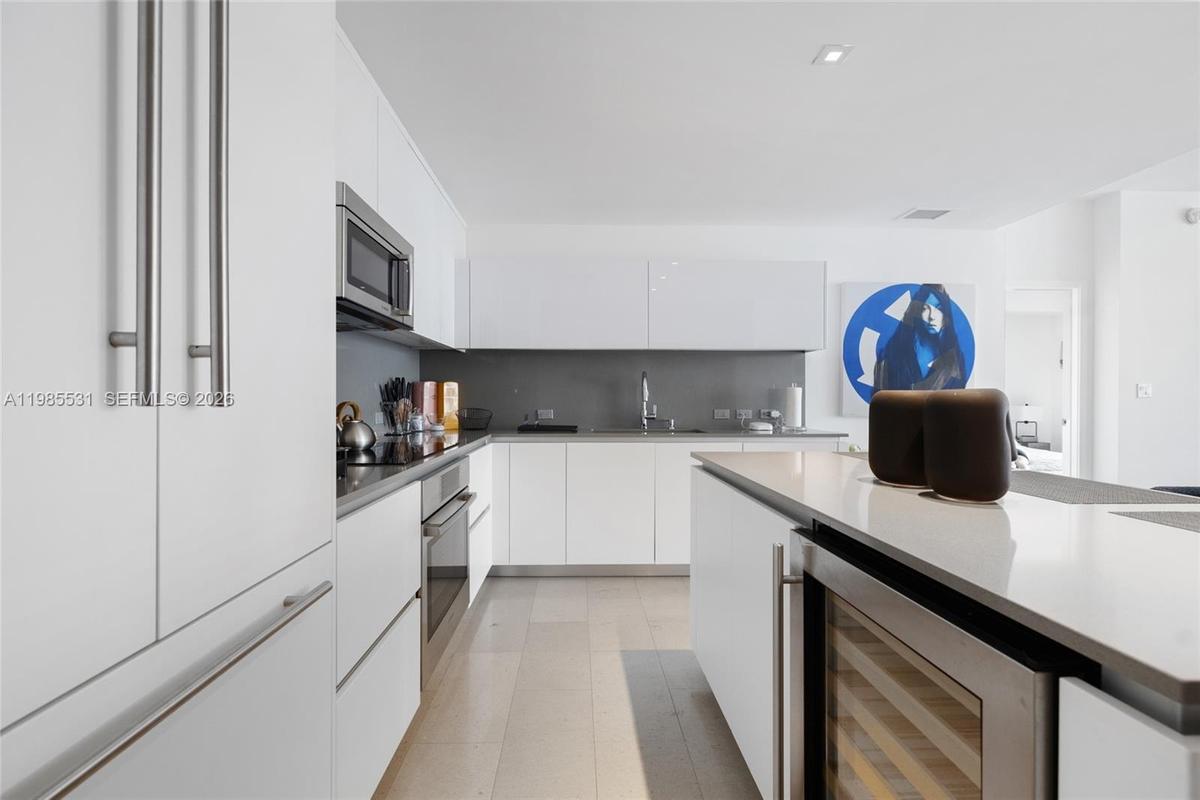 Kitchen featuring white flat-panel cabinetry, a central island with a solid surface countertop, neutral-toned backsplash, integrated appliances, and l