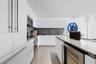 Kitchen featuring white flat-panel cabinetry, a central island with a solid surface countertop, neutral-toned backsplash, integrated appliances, and l