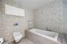 Walk-in shower featuring glass paneling, floor-to-ceiling mosaic tile surround, and wall-mounted plumbing fixtures, accompanied by a white floating va