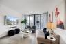 Open-concept interior featuring light-toned flooring, high ceilings, floor-to-ceiling windows with vertical blinds, and a kitchen equipped with flat-p