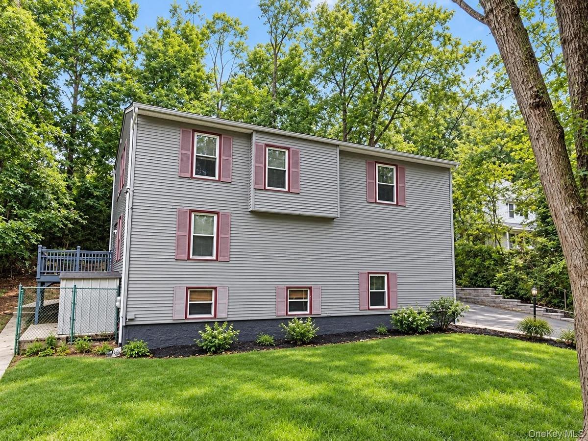 Exterior siding with multiple windows, a rear deck, a paved driveway, and established landscaping